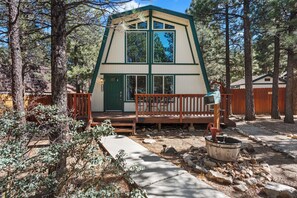 Una cabaña con terraza de madera, puerta verde y sendero de piedra.