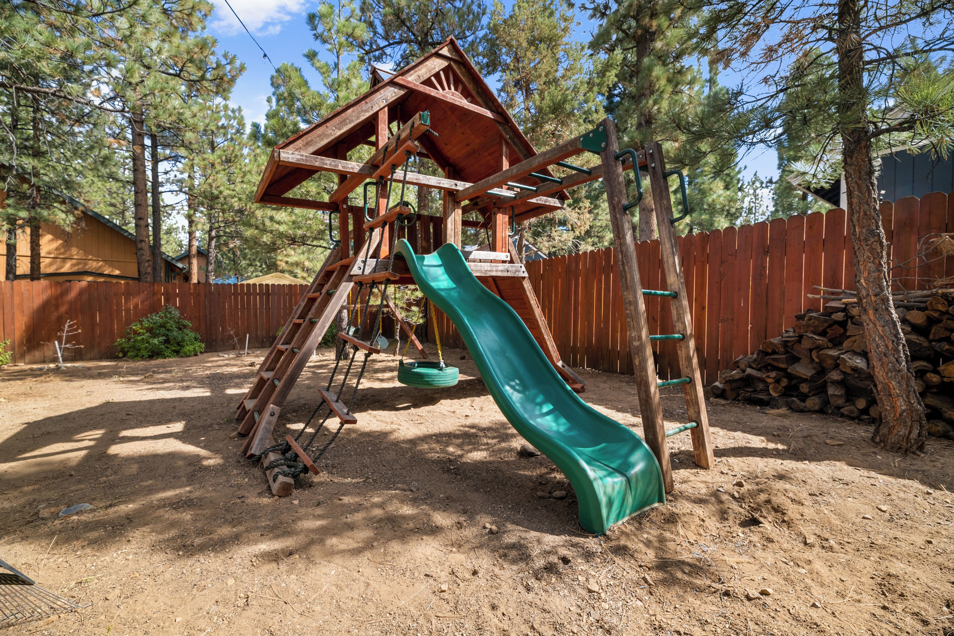 A wooden play structure with a slide and swings in a backyard.