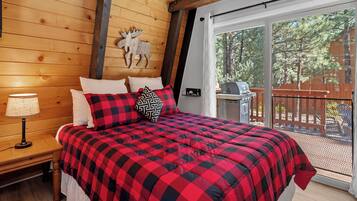 A bedroom with a large bed, a wooden headboard, a nightstand with a lamp, and a view of the outdoors through a sliding glass door.