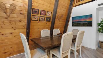 Un comedor con paneles de madera, una mesa de madera y seis sillas, un cuadro en la pared y fotografías enmarcadas.