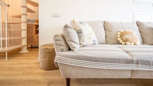 A cozy living room with a striped sofa, a woven ottoman, and a wooden staircase. - GuestReady - Beachfront dream in Sesimbra (Sesimbra)
