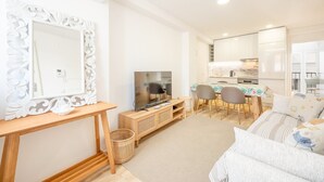 A modern living room with a TV, wooden furniture, a dining area, and a kitchen. - GuestReady - Beachfront dream in Sesimbra (Sesimbra)