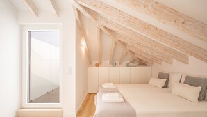 A bedroom with a sloped ceiling, a bed with pillows, a nightstand, and a wardrobe. - GuestReady - Beachfront dream in Sesimbra (Sesimbra)