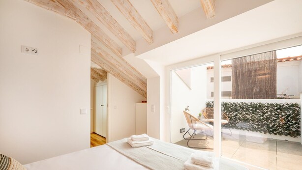 A modern bedroom with a large bed, a wooden ceiling, and a sliding glass door leading to a balcony with a view of the city. - GuestReady - Beachfront dream in Sesimbra (Sesimbra)