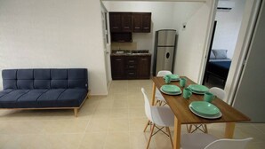 Un espacio habitable compacto con sofá, mesa de comedor, sillas, zona de cocina con armarios y refrigerador.