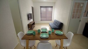 Un comedor con una mesa de madera, sillas blancas y un sofá gris.