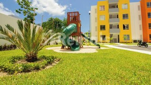 A playground with a slide and a climbing structure, surrounded by a well-maintained lawn and palm trees. - Apartment With Pool In Playa Del Carmen (Playa del Carmen)