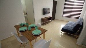 A dining area with a wooden table, white chairs, and a TV on a stand. - Apartment With Pool In Playa Del Carmen (Playa del Carmen)