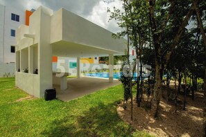 A modern building with a covered outdoor area, a pool, and a tree. - Apartment With Pool In Playa Del Carmen (Playa del Carmen)