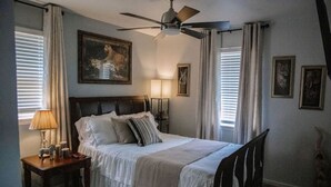 A bedroom with a bed, a nightstand, a ceiling fan, and a painting on the wall.