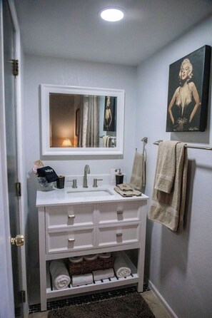 A bathroom with a white vanity, a mirror, a towel rack, and a framed picture on the wall. - LET D'S COZY COTTAGE #2 PROVIDE YOU A COMFORTABLE STAY IN BIG SPRING, TEXAS!!! (Big Spring)