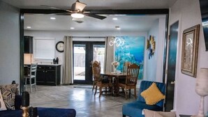 A spacious living area with a dining table, blue sofa, and a ceiling fan.