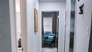 A narrow hallway with a wooden floor, a blue sofa in the background, and a door on the right.