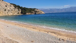 Une plage à l’eau claire, avec un rivage de galets et une falaise rocheuse.