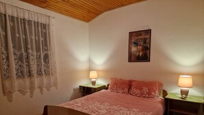 Une chambre à coucher avec un lit, deux lampes de chevet, un tableau au mur, une fenêtre avec des rideaux et un plafond en bois.