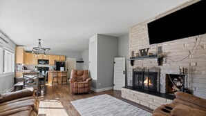 A modern living room with a fireplace, a sofa, and a kitchen in the background. - Woodburn.  (Spearfish)