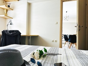 A bedroom with a bed, a desk, a chair, and a door leading to a dining area. - Cozy Snuggle- 2min To Beach, 6min Walk To Old Town (Chania)