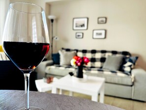 A glass of red wine on a table with a checkered sofa and a white coffee table in the background. - Cozy Snuggle- 2min To Beach, 6min Walk To Old Town (Chania)
