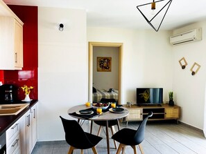 A modern kitchen with a dining area, a TV, and a red accent wall. - Cozy Snuggle- 2min To Beach, 6min Walk To Old Town (Chania)