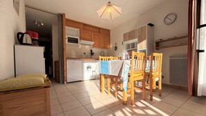 A compact kitchen with wooden cabinets, a dining table with chairs, a washing machine, and a refrigerator.