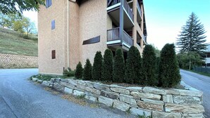 A multi-story building with a stone retaining wall and neatly trimmed evergreen trees in front.