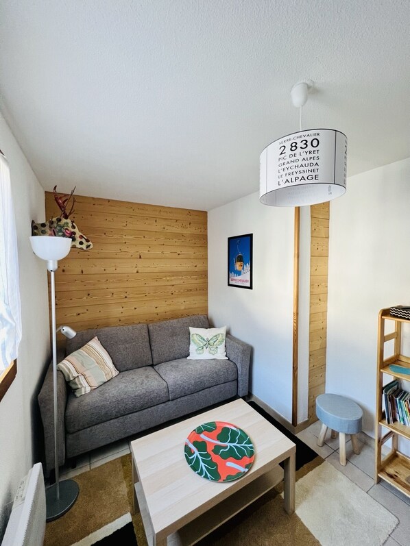 A modern living room with a grey sofa, a wooden accent wall, a floor lamp, a small side table, and a bookshelf.