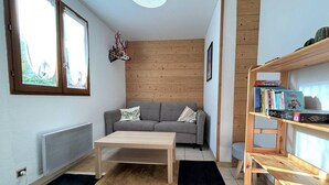 A cozy living room with a grey sofa, a wooden coffee table, a bookshelf with books, a decorative deer head, and a radiator.