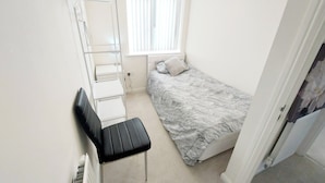 Un dormitorio pequeño y funcional con una cama individual, un escritorio y una silla.