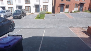 Un aparcamiento con varios coches, un edificio de ladrillo y una pequeña zona verde.