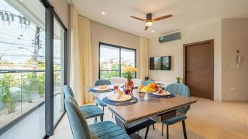 A dining area with a table set for four, chairs, a ceiling fan, and a view through large windows.