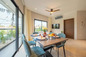 A dining area with a table set for four, chairs, a ceiling fan, and a view through large windows.