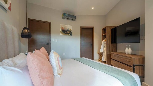 A hotel room with a bed, a TV, a wardrobe, and a painting on the wall. - Kippal Onix |Luxurious 2-Bedroom Cozumel Apartment (San Miguel de Cozumel)
