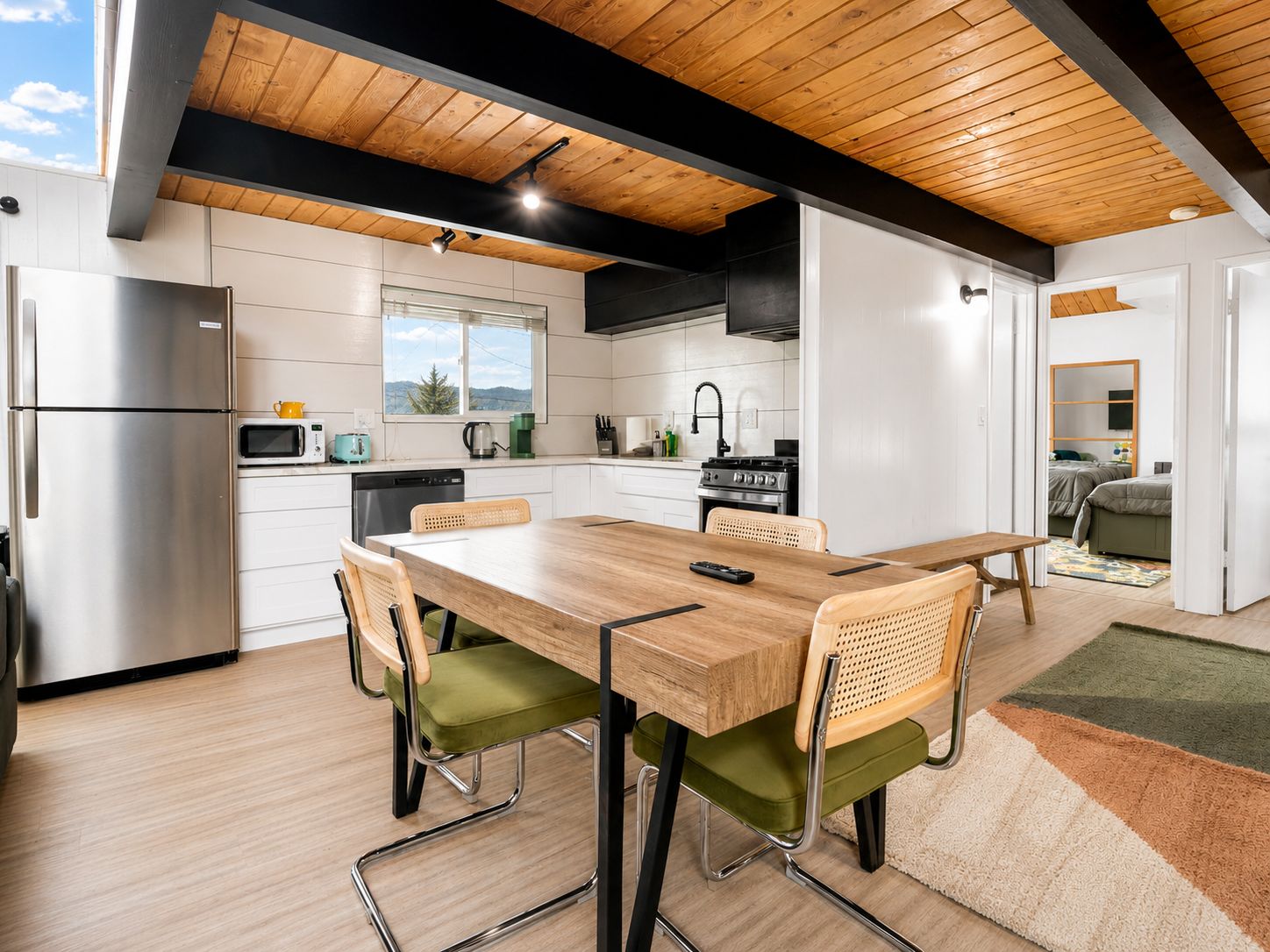 A modern kitchen with white cabinets, a wooden dining table, and a view of the outdoors.