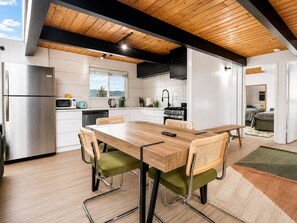 A modern kitchen with white cabinets, a wooden dining table, and a view of the outdoors. - Big Bear Lake View (Big Bear Lake)