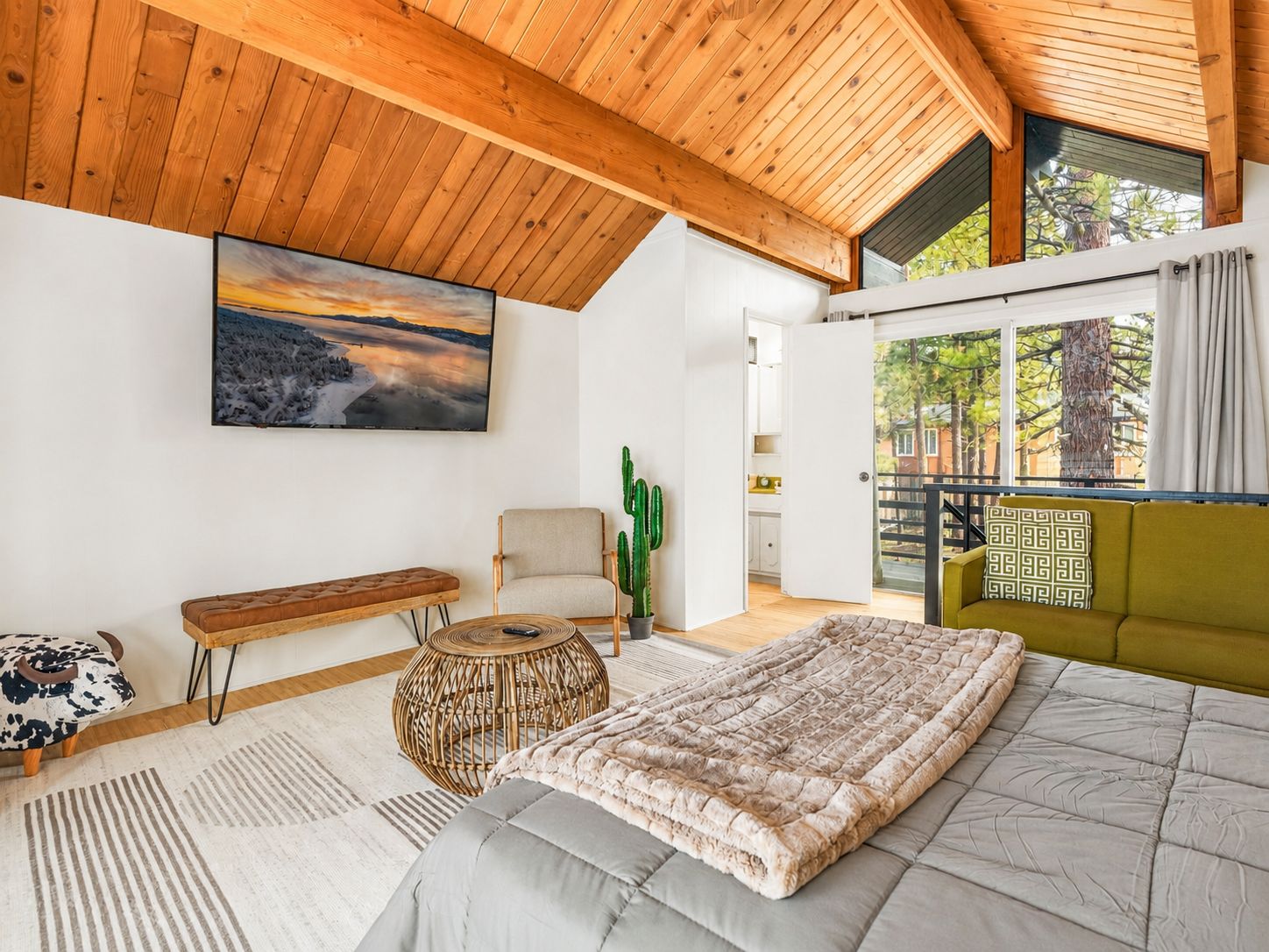 A modern bedroom with a large bed, a bench, a chair, and a cactus.