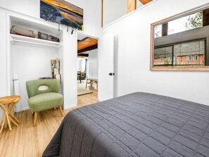 A bedroom with a bed, a green chair, a wooden table, and a window with a view of a building. - Big Bear Lake View (Big Bear Lake)