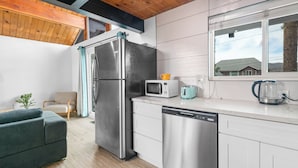 Una cocina moderna con un refrigerador de acero inoxidable, microondas y lavavajillas, un tostador color turquesa y una ventana con vista a una casa.