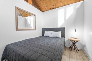 A bedroom with a bed, a bedside table, a lamp, and a mirror on the wall. - Big Bear Lake View (Big Bear Lake)