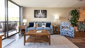 A living room with a sofa, a coffee table, a patterned armchair, a large plant, and a wall art piece.
