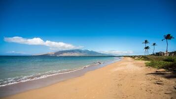 Di pantai, pasir putih, payung pantai, dan handuk pantai