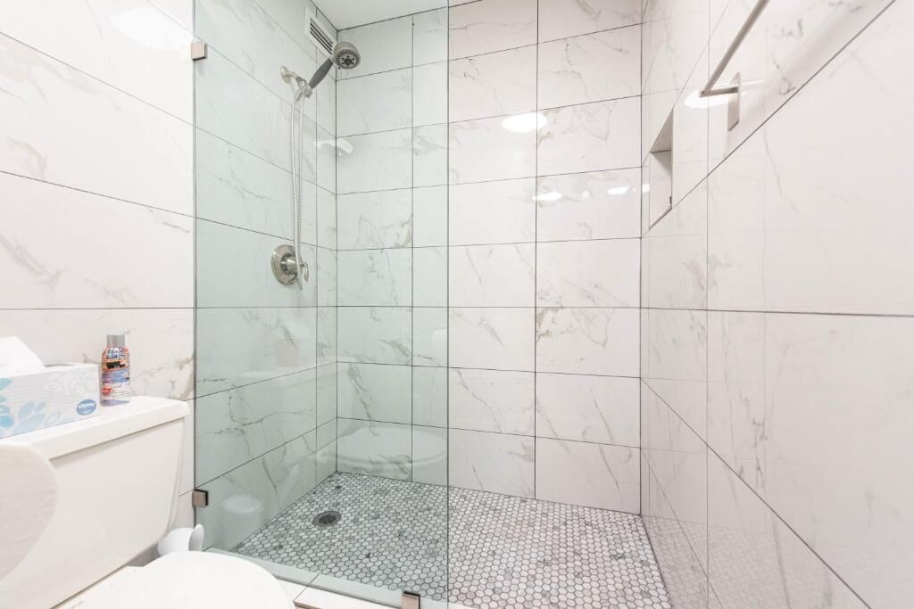 Une salle de bain moderne avec une douche en verre, des carreaux de marbre blanc et des toilettes dotées d’un porte-mouchoirs.