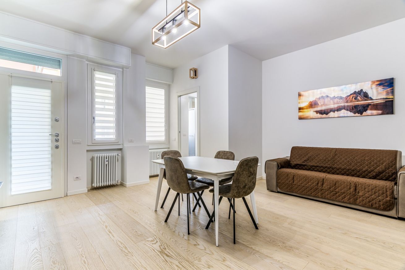 A modern living room with a white dining table, brown sofa, and a painting on the wall.