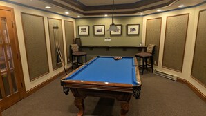 Une table de billard dans une pièce dont le sol est recouvert de moquette, dotée d’un éclairage encastré et ornée de tableaux encadrés aux murs.