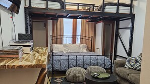 Une pièce de taille modeste comprenant un lit superposé, un bureau avec une chaise, un canapé et un tapis à motifs.
