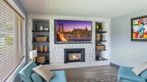 A modern living room with a fireplace, a flat-screen TV mounted on a textured wall, and two blue sofas. - Grand Oasis Kelowna, Resort-Style Pool, Hot Tub, Sauna 5 Min to Downtown (Kelowna)