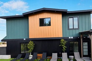 A modern two-story house with a flat roof, a large window on the upper floor, and a balcony with lounge chairs. - Grand Oasis Kelowna, Resort-Style Pool, Hot Tub, Sauna 5 Min to Downtown (Kelowna)