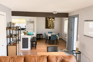 A modern living space with a dining area, kitchen, and a large window. - Grand Oasis Kelowna, Resort-Style Pool, Hot Tub, Sauna 5 Min to Downtown (Kelowna)