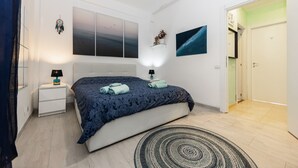 Een moderne slaapkamer met een groot bed, nachtkastjes, een wandplank en een deur naar een andere kamer.
