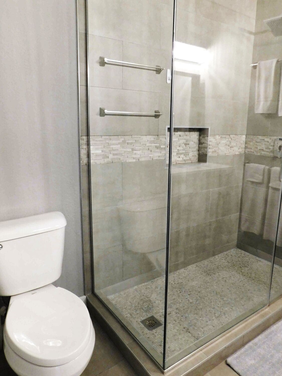 A modern bathroom with a glass-enclosed shower, a white toilet, and a tiled backsplash.