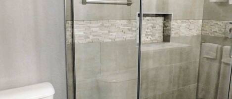 A modern bathroom with a glass-enclosed shower, a white toilet, and a tiled backsplash.
